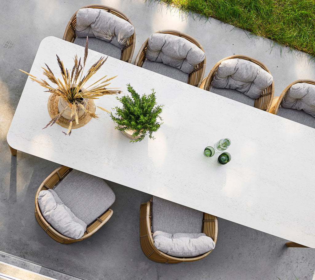 A long, elegant table surrounded by stylish chairs, adorned with a decorative plant and glass bottles on top.