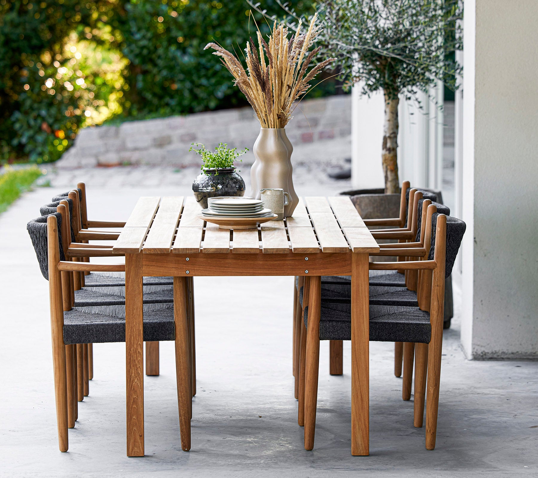 A wooden table surrounded by eight stylish chairs, adorned with a vase and greenery, creating an inviting dining space.