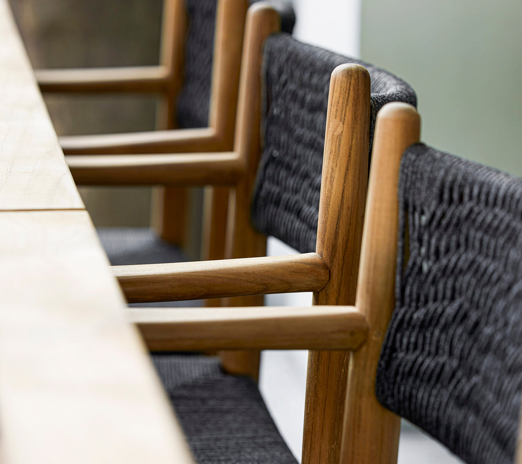 A close-up of modern wooden chairs with woven black textile details, arranged neatly beside a long wooden table.