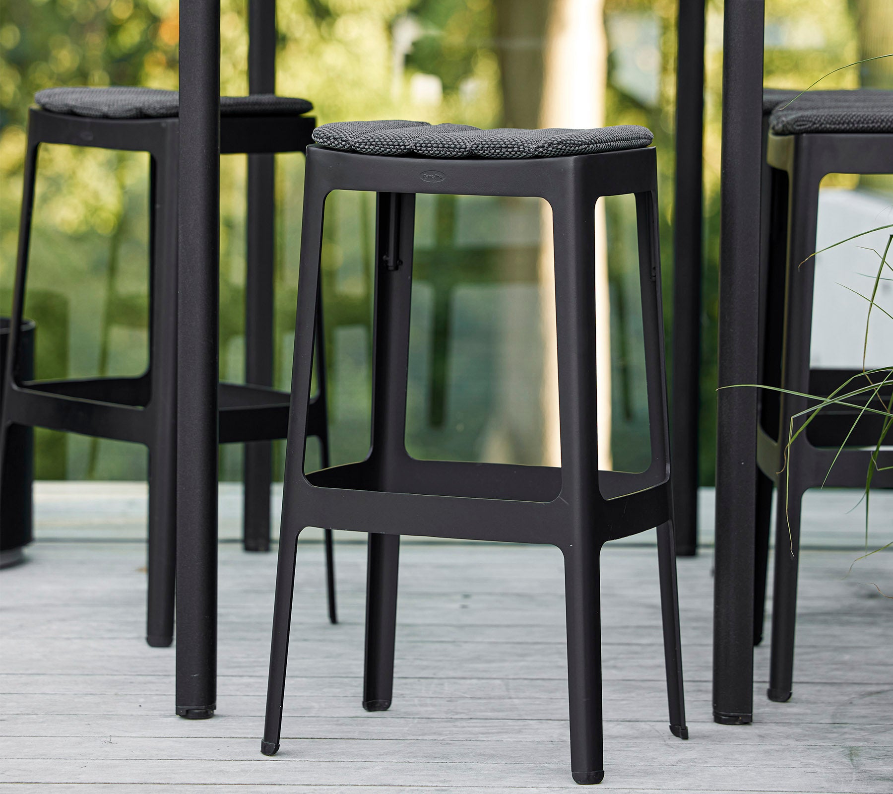 Black bar stools with a minimalist design and cushioned seats, arranged closely together, showcasing a modern aesthetic.