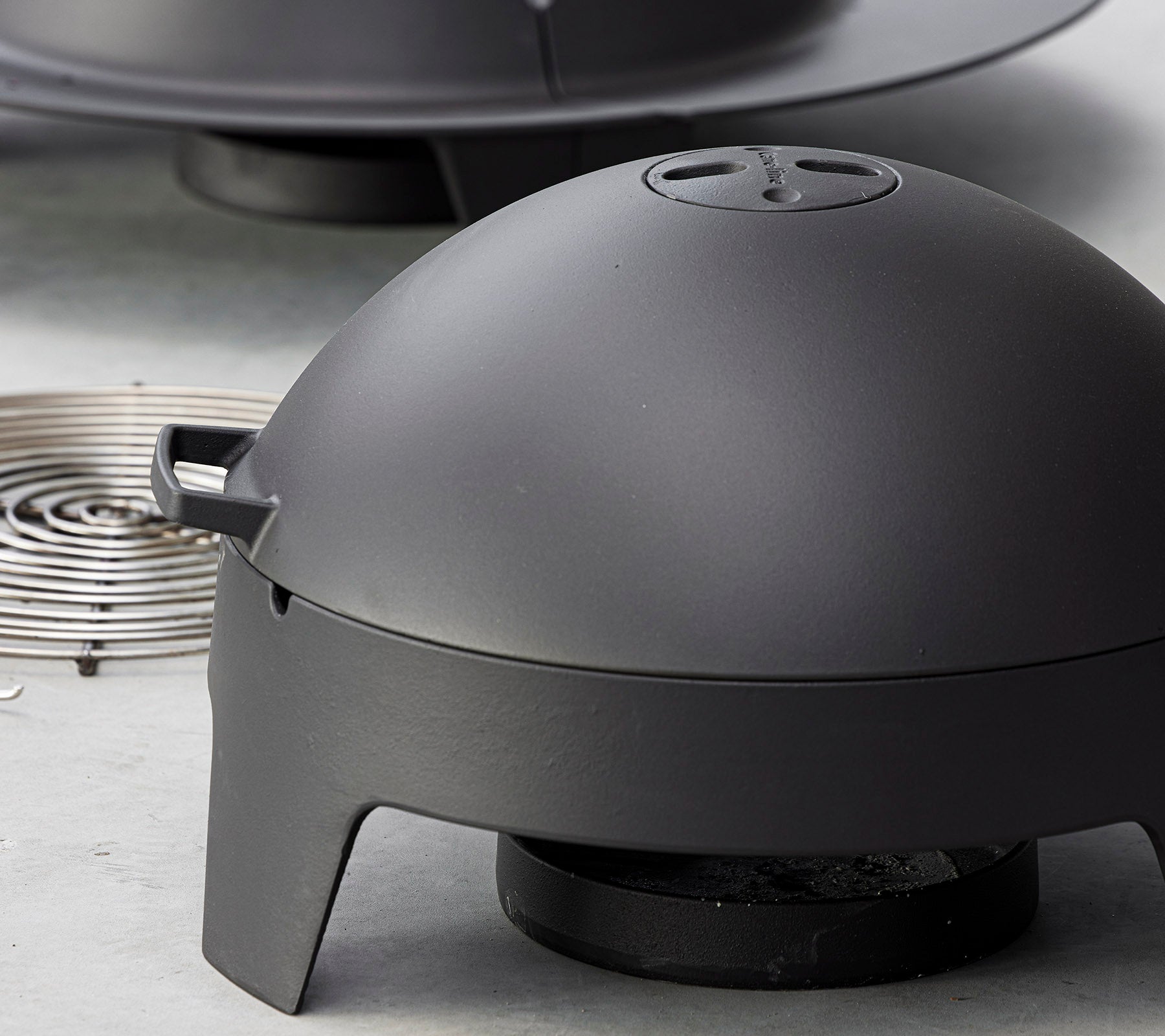 Matte black cooking appliance with a dome-shaped lid and a removable heat source, designed for outdoor grilling and barbecuing.