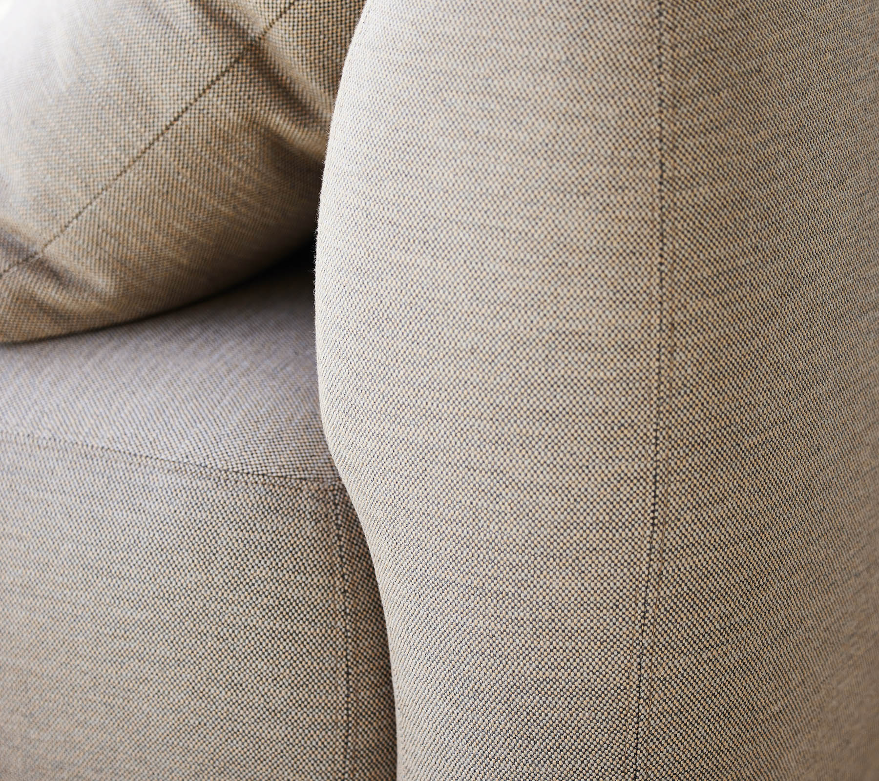 Close-up of a textured beige upholstery, highlighting the curved armrest and soft cushions of a furniture piece.