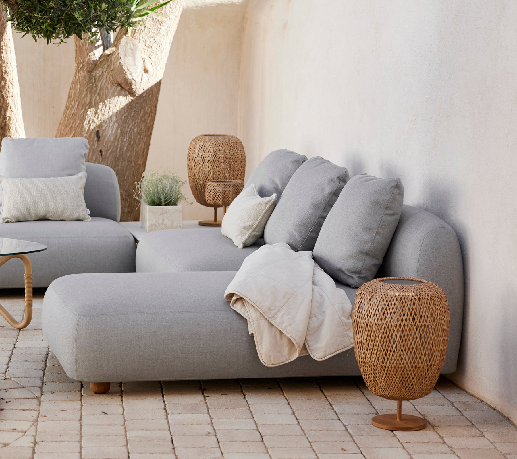 Modern grey sofa with cushions and a woven side table in a minimalist lounge setting.