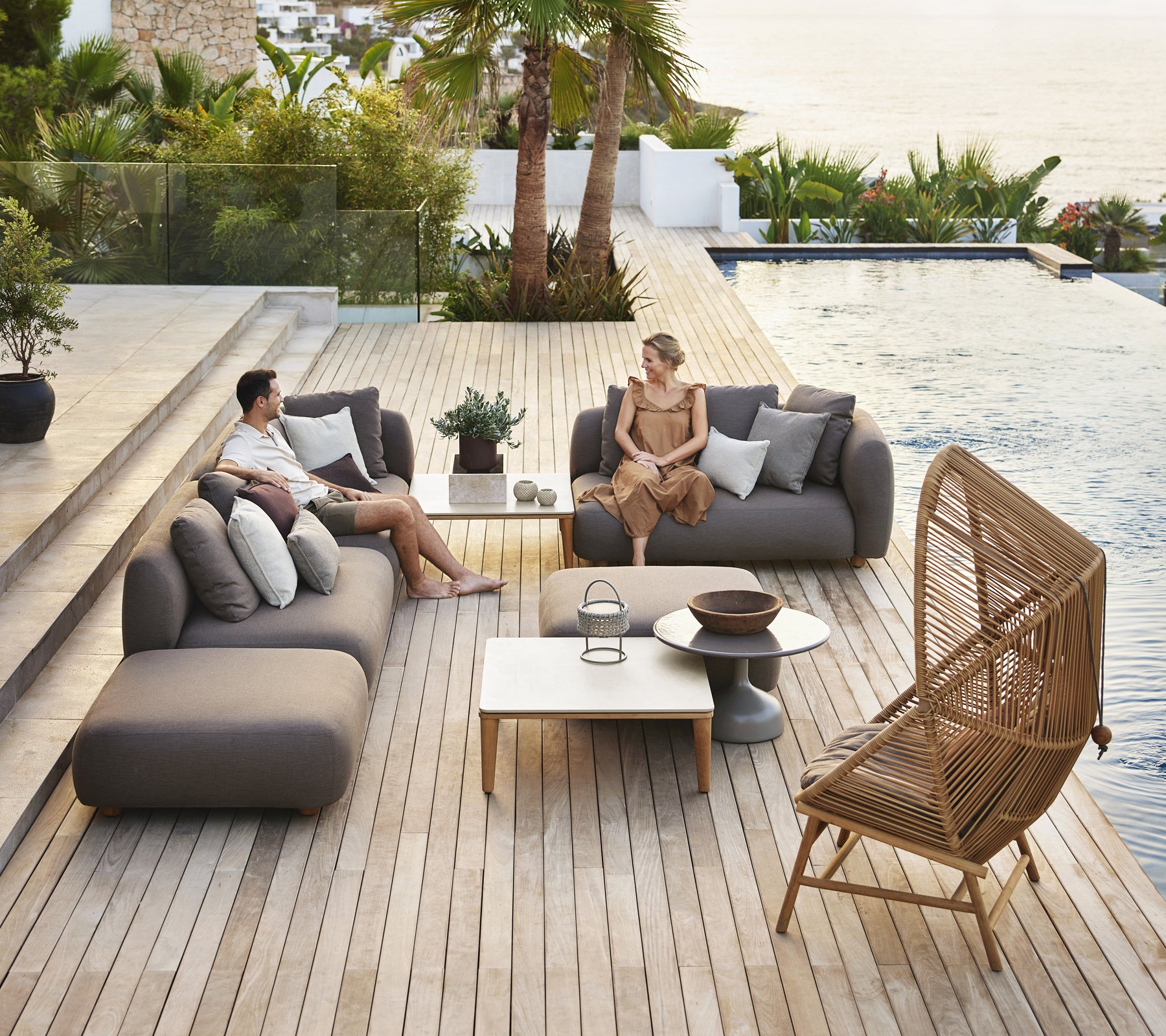 Modern outdoor lounge area featuring grey sofas, a white table, and a rattan chair.