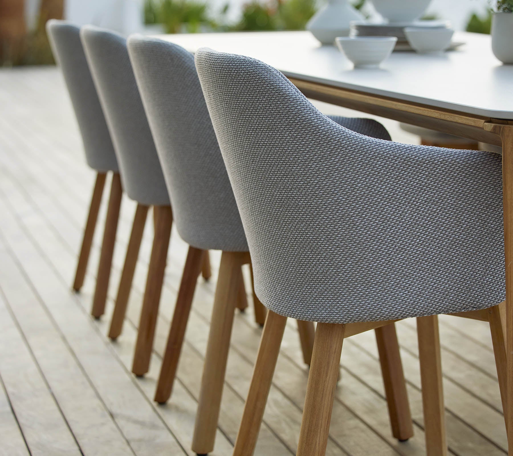 A row of modern upholstered chairs with wooden legs arranged neatly beside a table, showcasing a stylish and contemporary design.