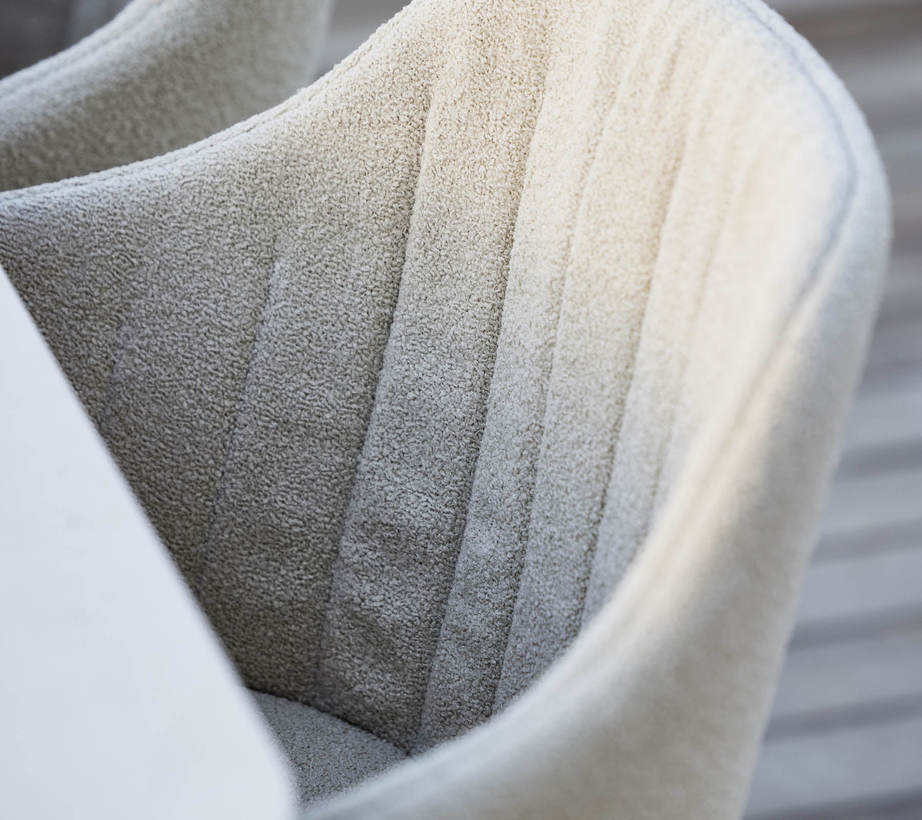 Textured, fully upholstered chair with subtle vertical stitching, showcasing a soft, neutral color and a modern design aesthetic.