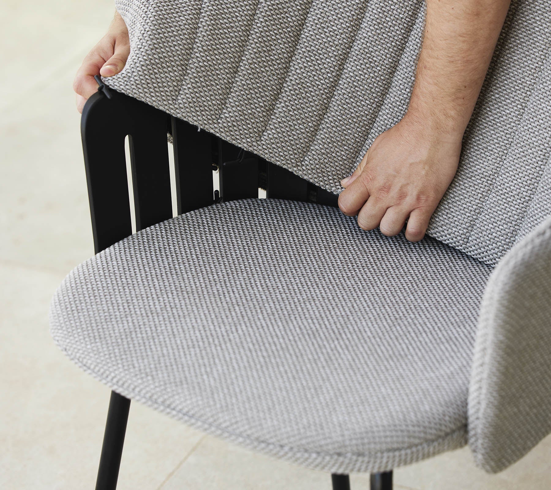 Person adjusting the back of a modern chair with a textured fabric seat, showcasing a stylish design and ergonomic support.