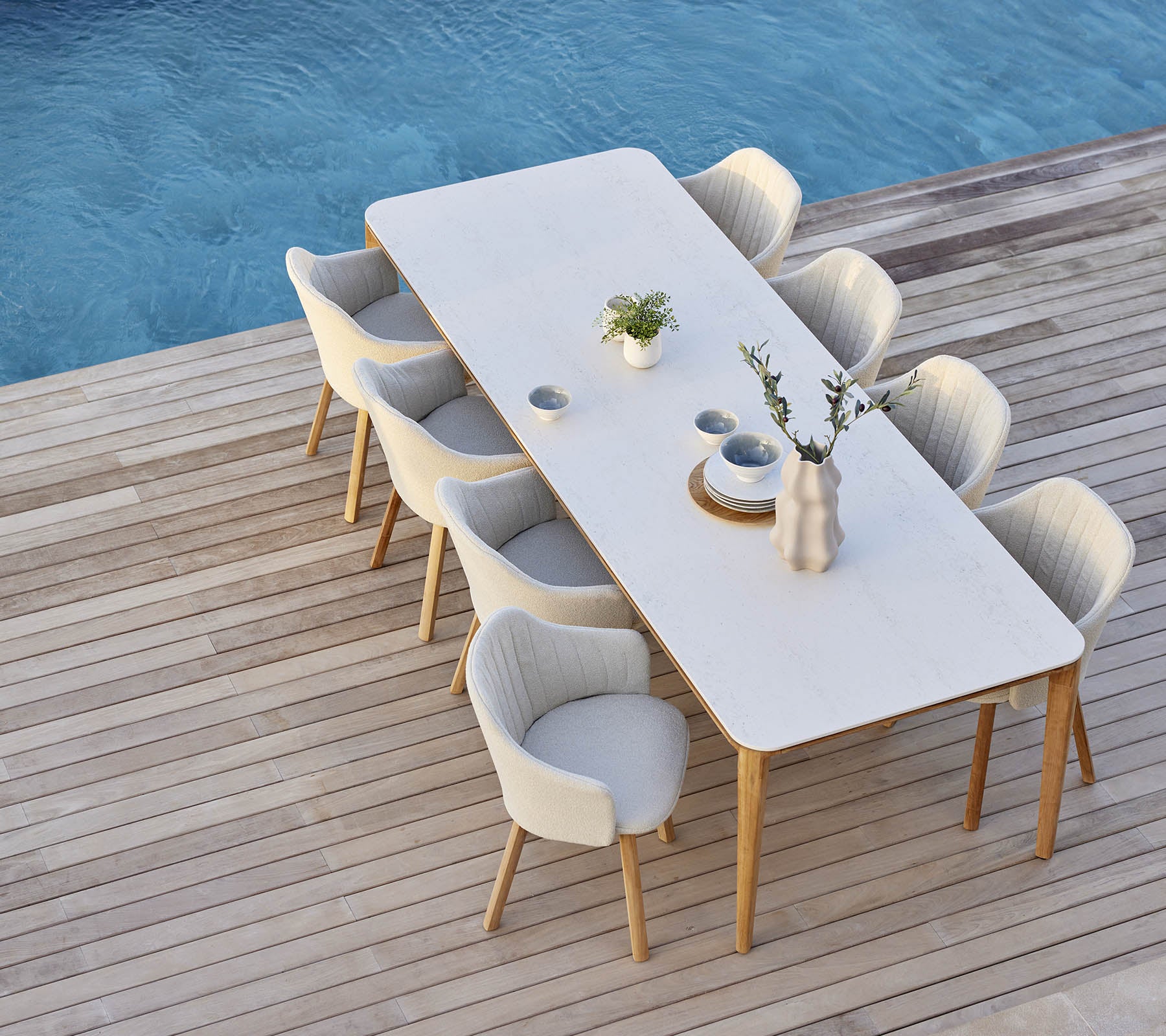 Elegant dining setup featuring a long table surrounded by comfortable chairs, adorned with a vase and plant accents.