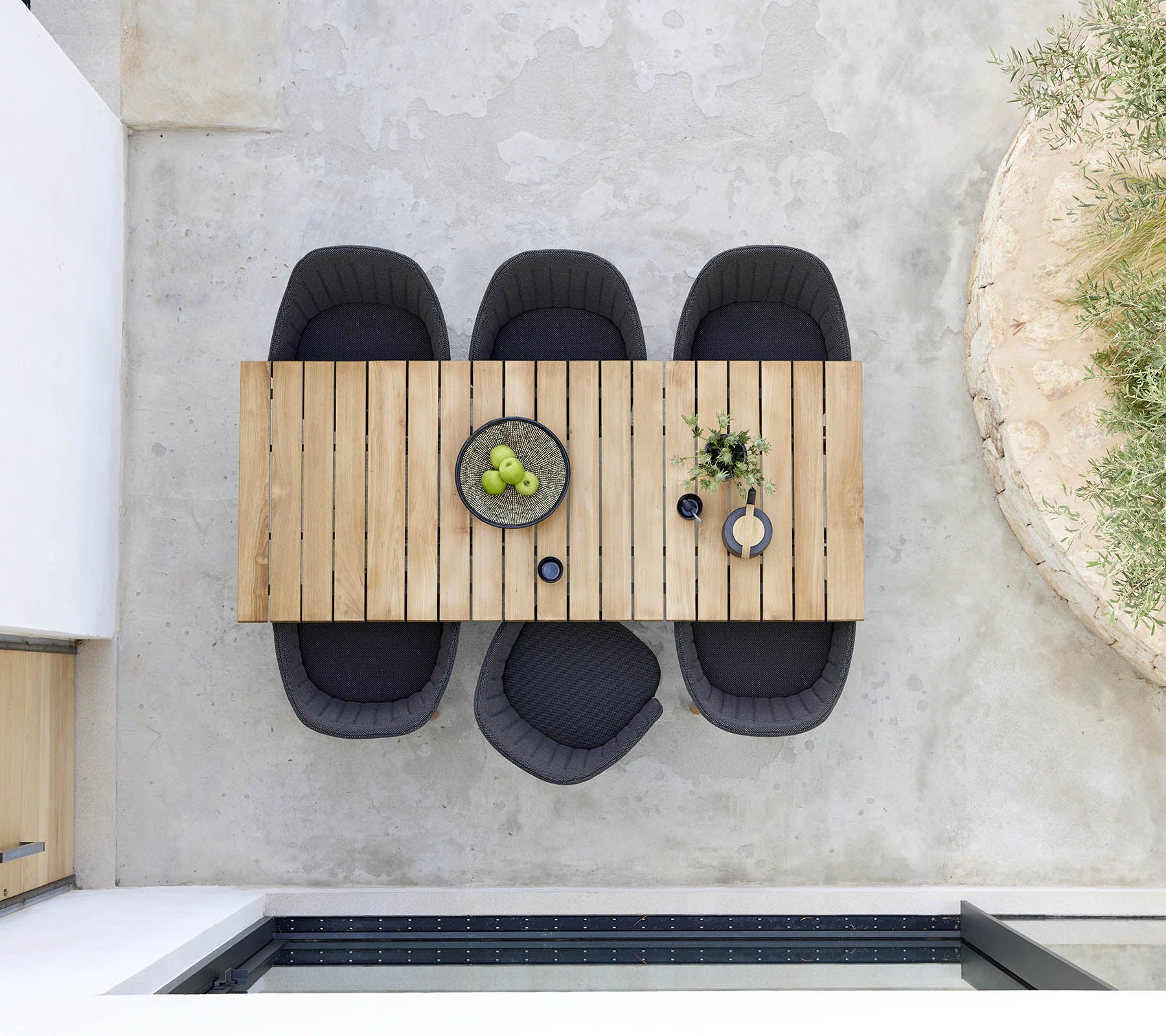 Stylish wooden dining table accompanied by four black chairs, featuring a bowl of green fruit and decorative plants for a modern touch.
