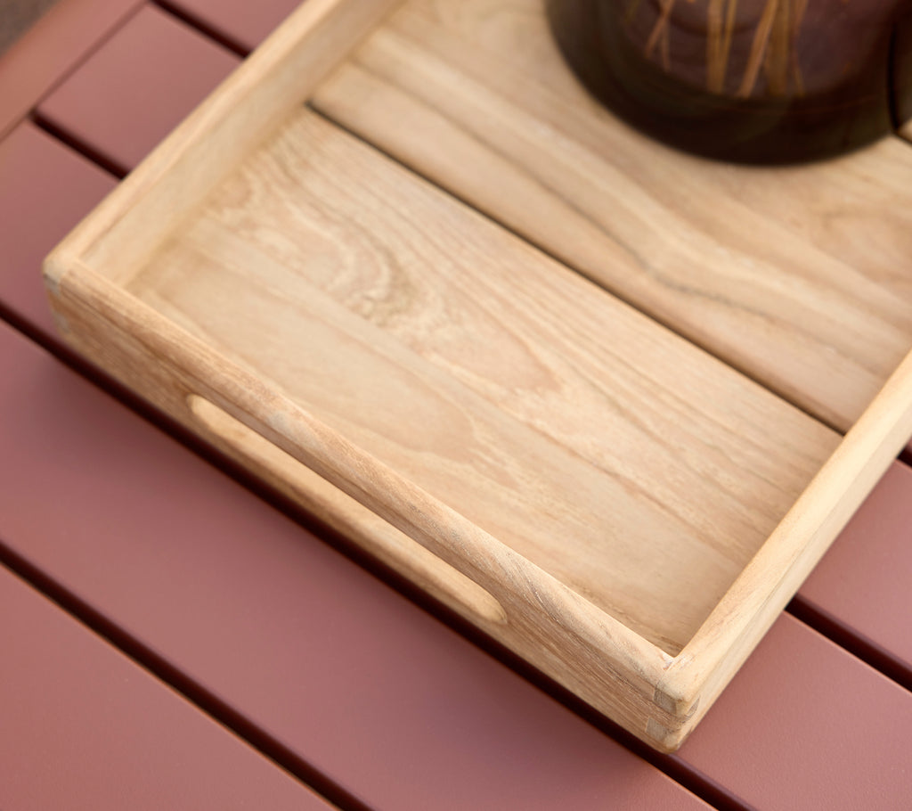 A light wooden tray with a natural finish on a pastel pink surface.