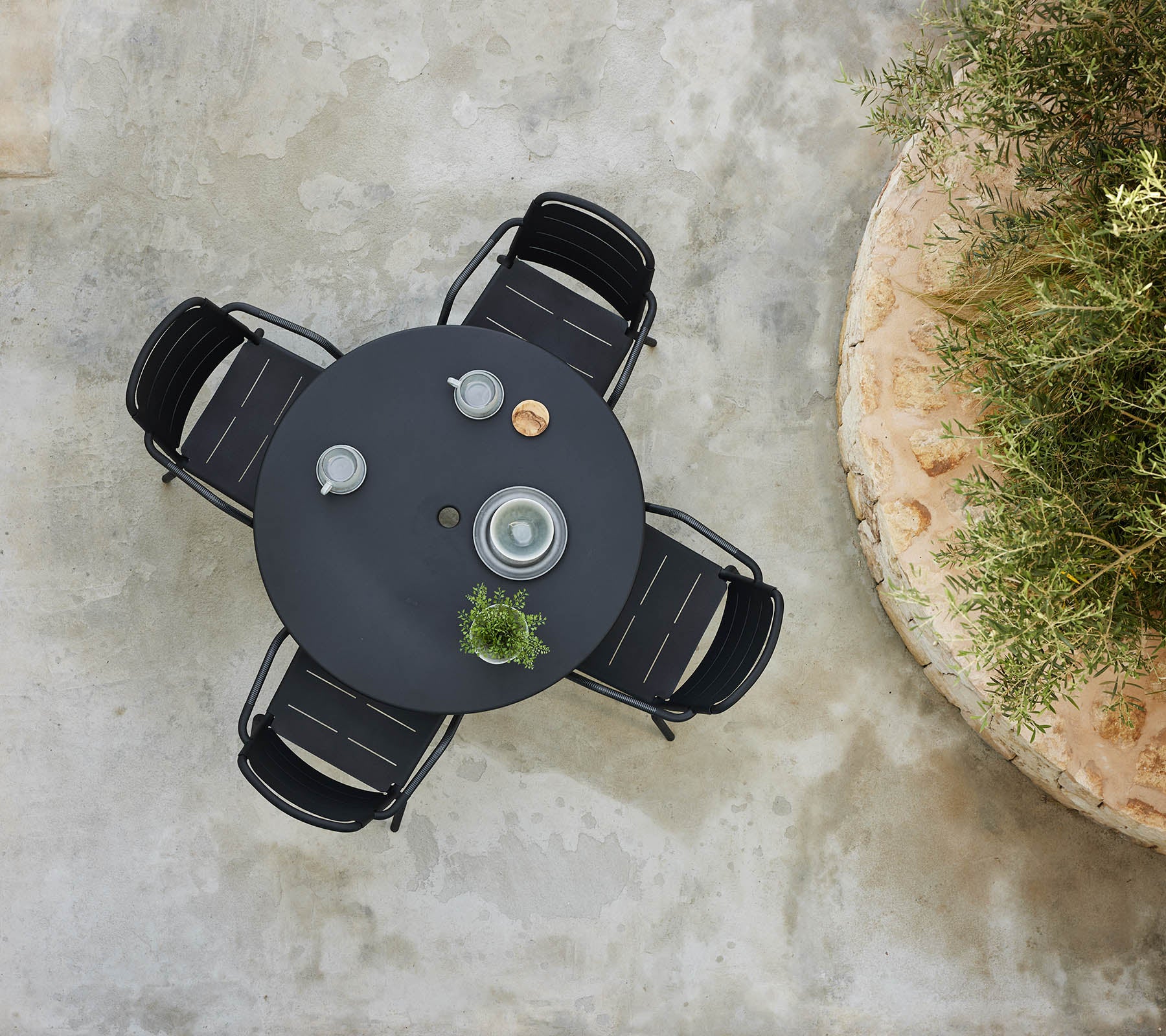 A top-down view of a round area table surrounded by Copenhagen chairs, featuring decorative items and a small plant.