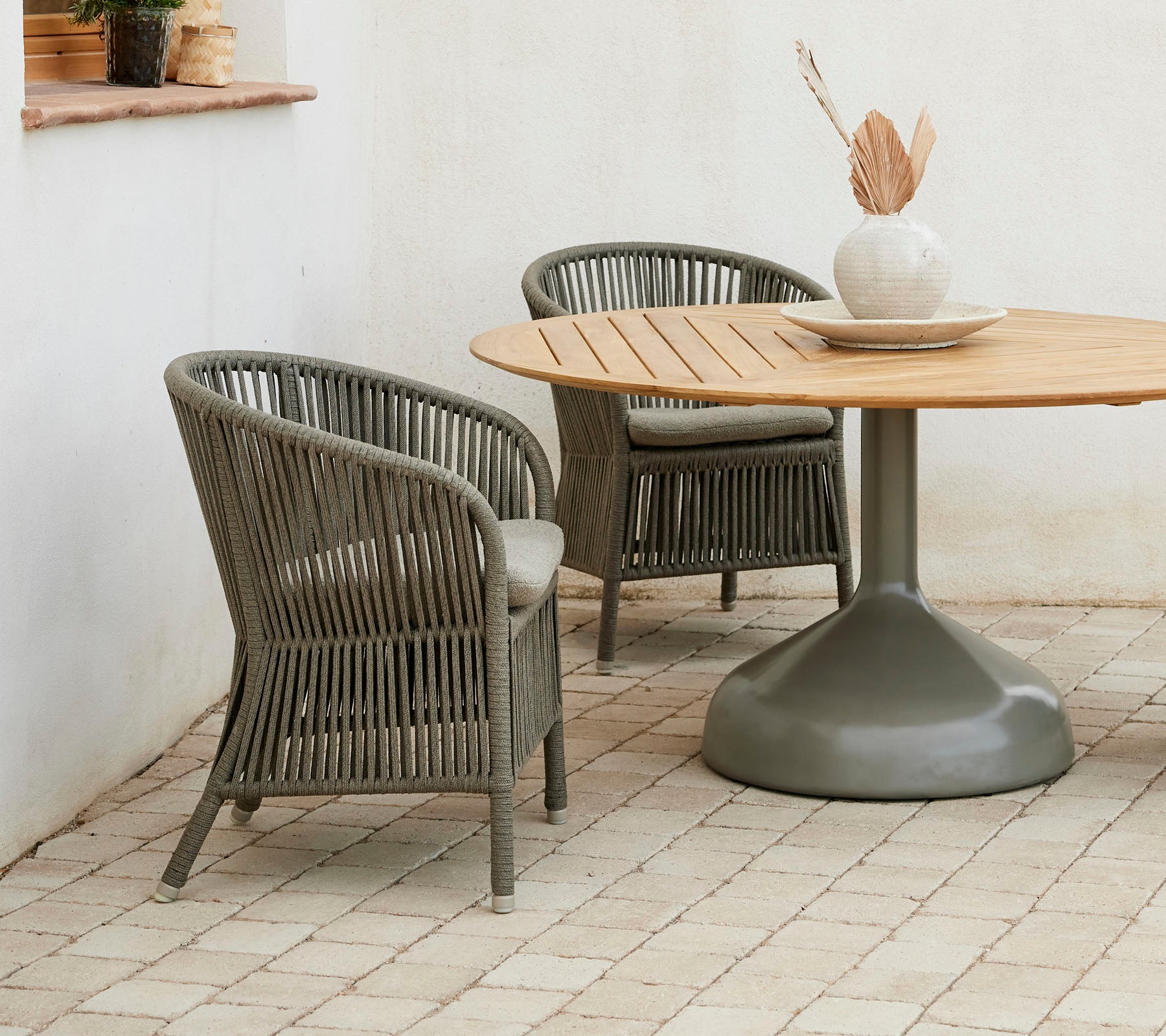 Two stylish Derby chairs paired with a round Glaze dining table, featuring a neutral color palette and a decorative vase.