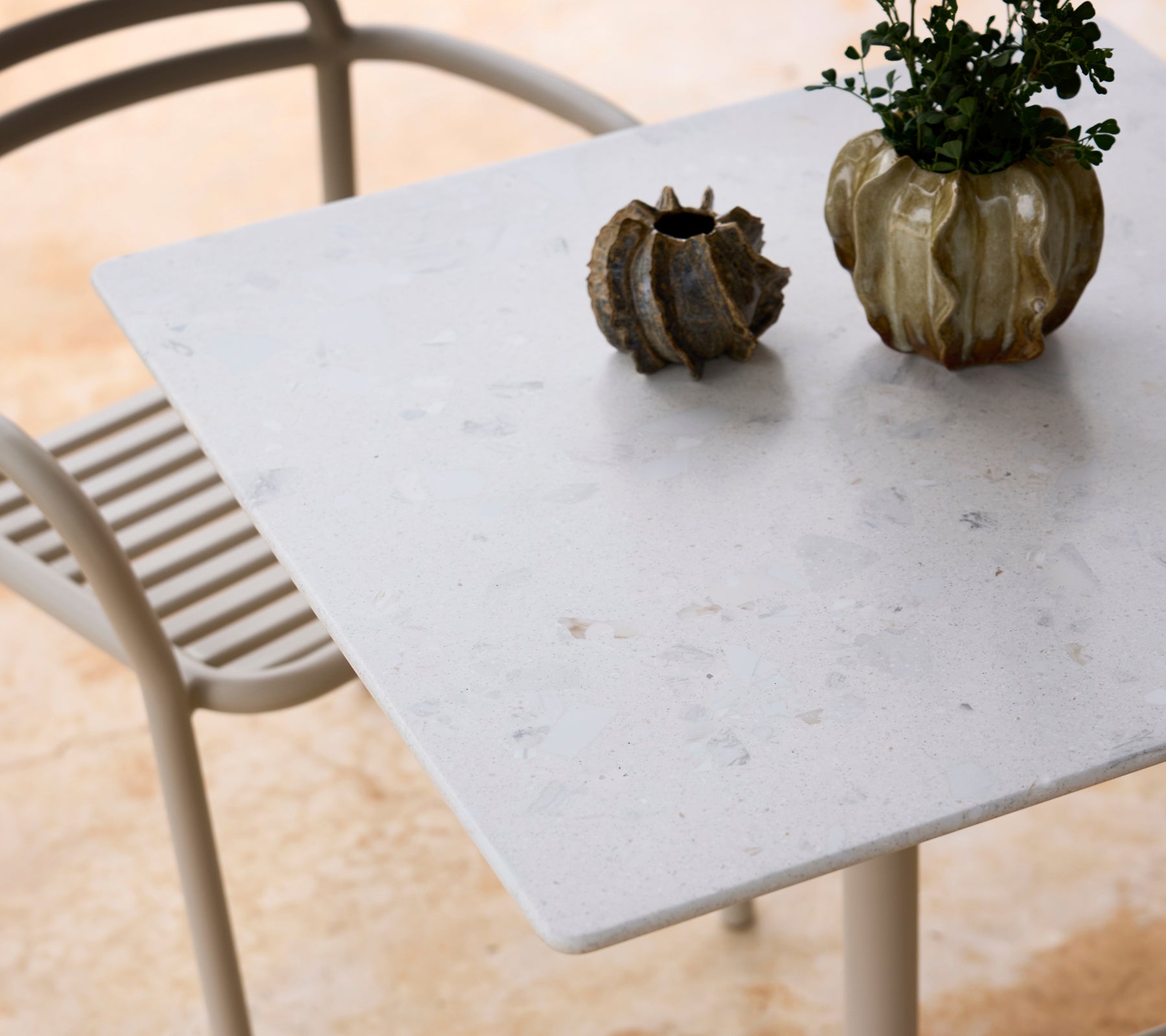 White table with a grey chair and a green plant centerpiece.