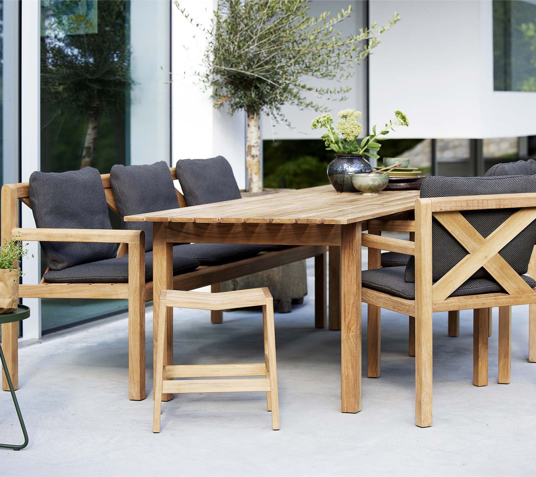 A wooden table surrounded by stylish chairs and a bench, featuring soft cushions and decorative plants for an inviting seating area.