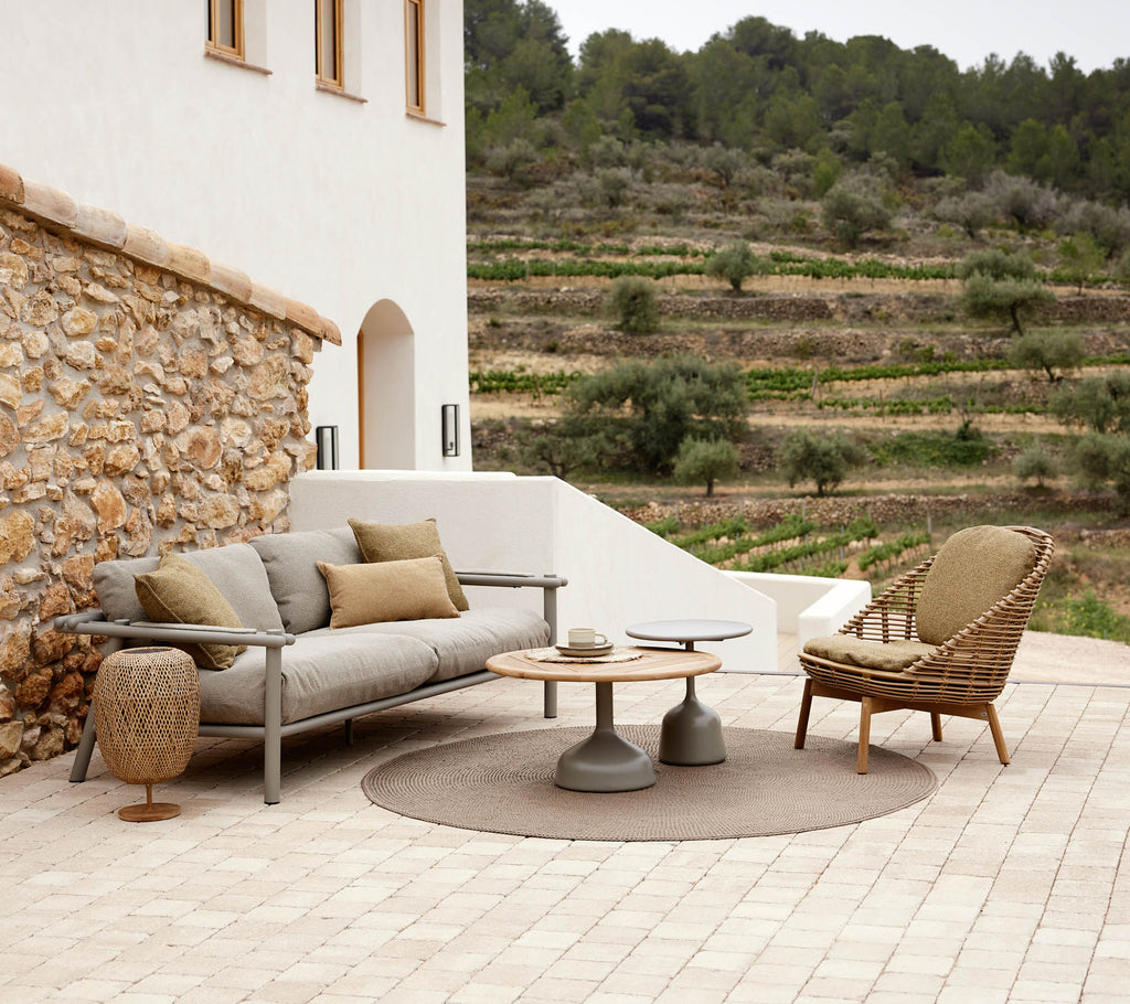 A Hive lounge chair and Sticks sofa arranged with a round table and decorative elements, set against a serene landscape.