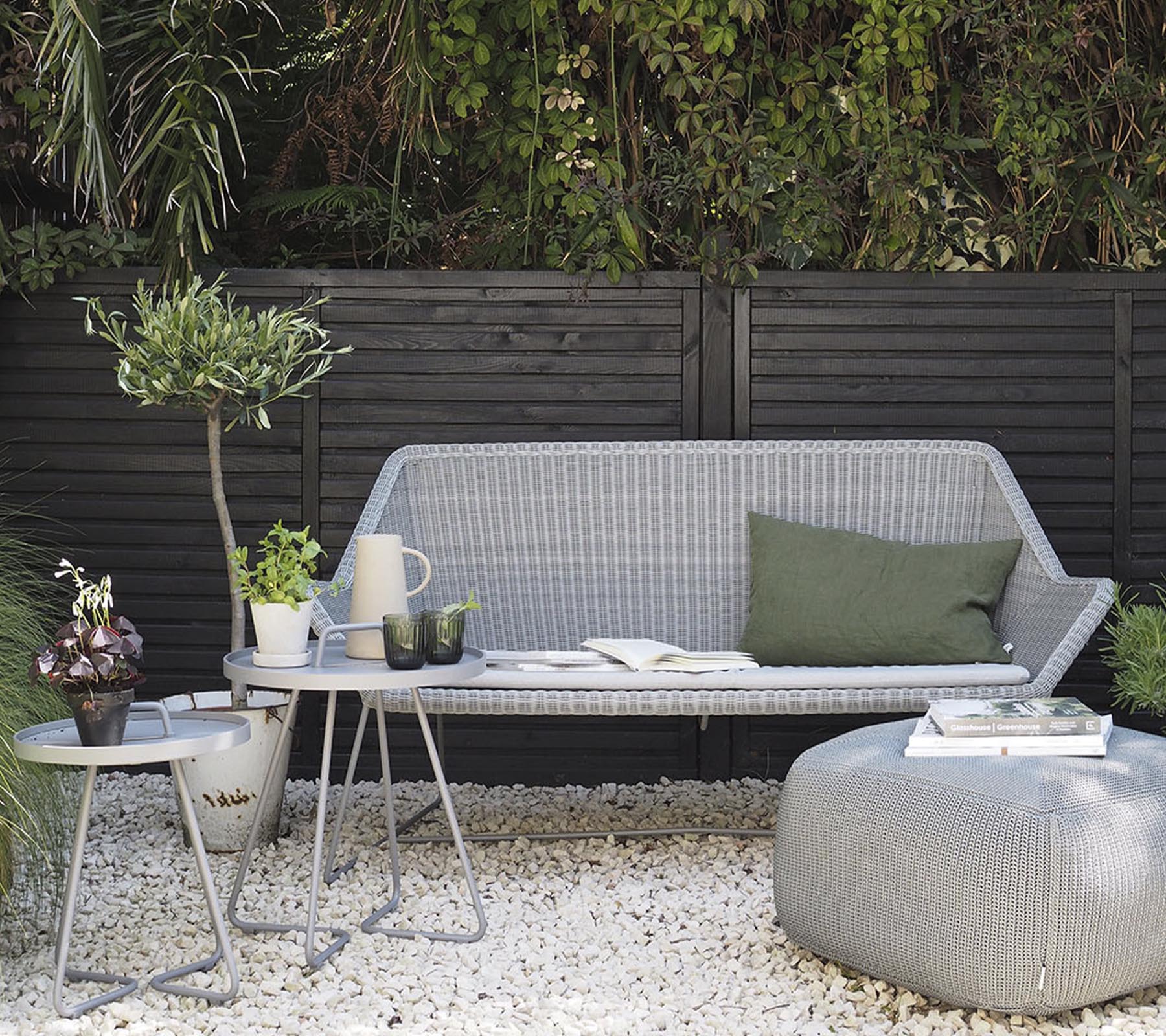 Minimalist outdoor furniture arrangement featuring a stylish sofa, side tables, and decorative plants on a pebble surface.