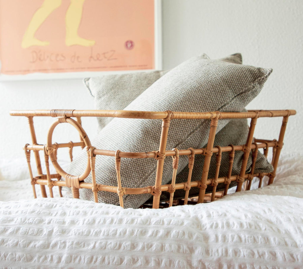 Rattan basket with grey and white pillows in a cozy bedroom setting.