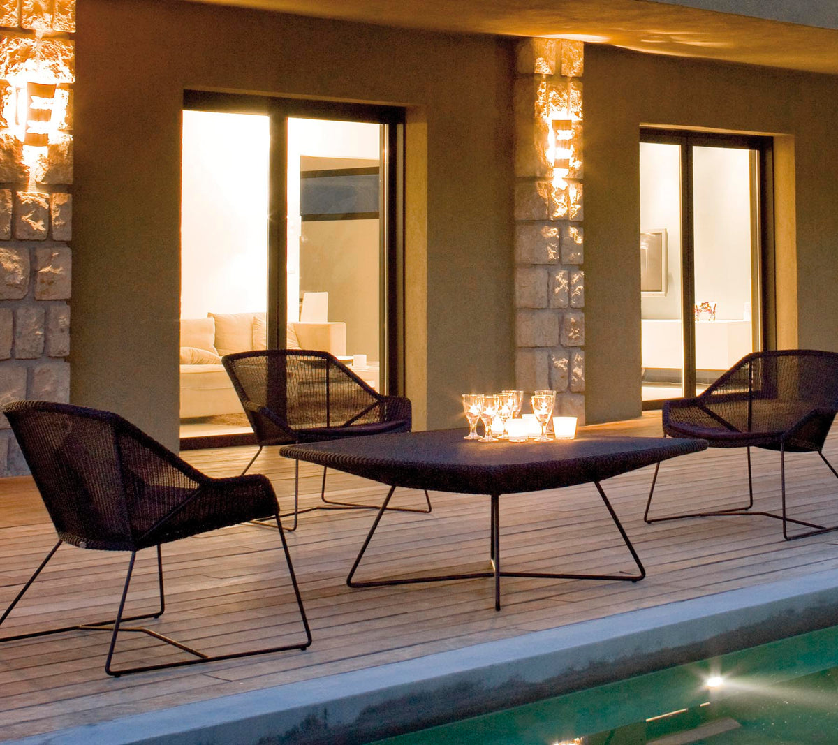 A stylish lounge seating arrangement featuring four black mesh chairs around a sleek table, illuminated by soft ambient lighting.