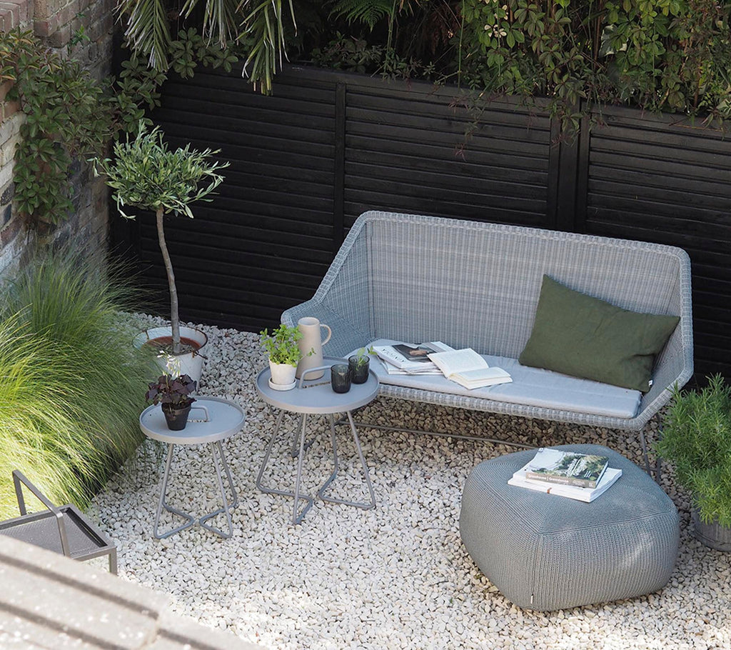 Modern grey sofa with green cushion and grey side table in a minimalist lounge area.