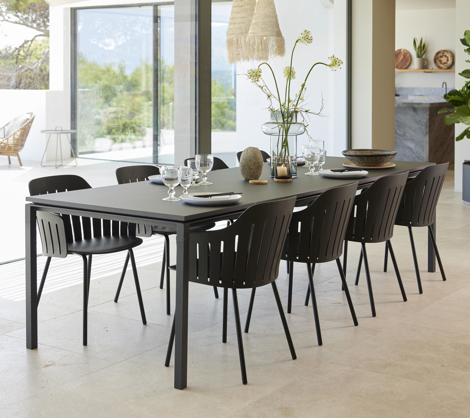 A stylish dining table set with eight black chairs, elegantly arranged with tableware and a vase of flowers as the centerpiece.