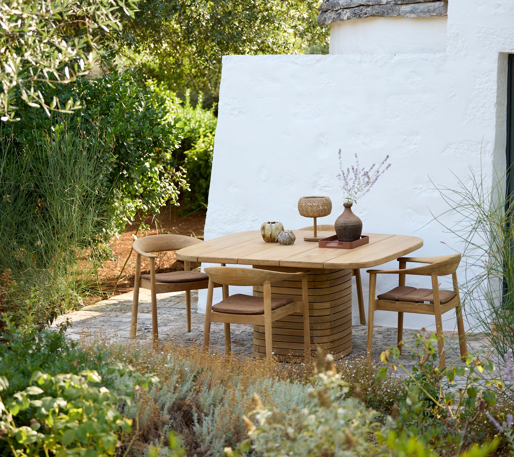 Modern round table with wooden chairs and decorative vase in an outdoor setting.