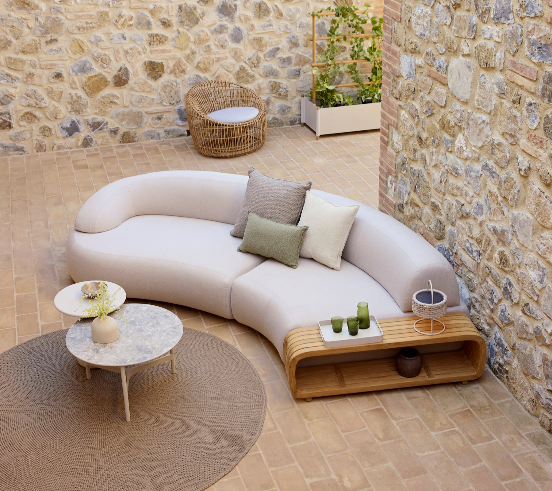 Curved mellow sofa with decorative cushions, a mellow coffee table, and a round nest chair, set on a textured floor.