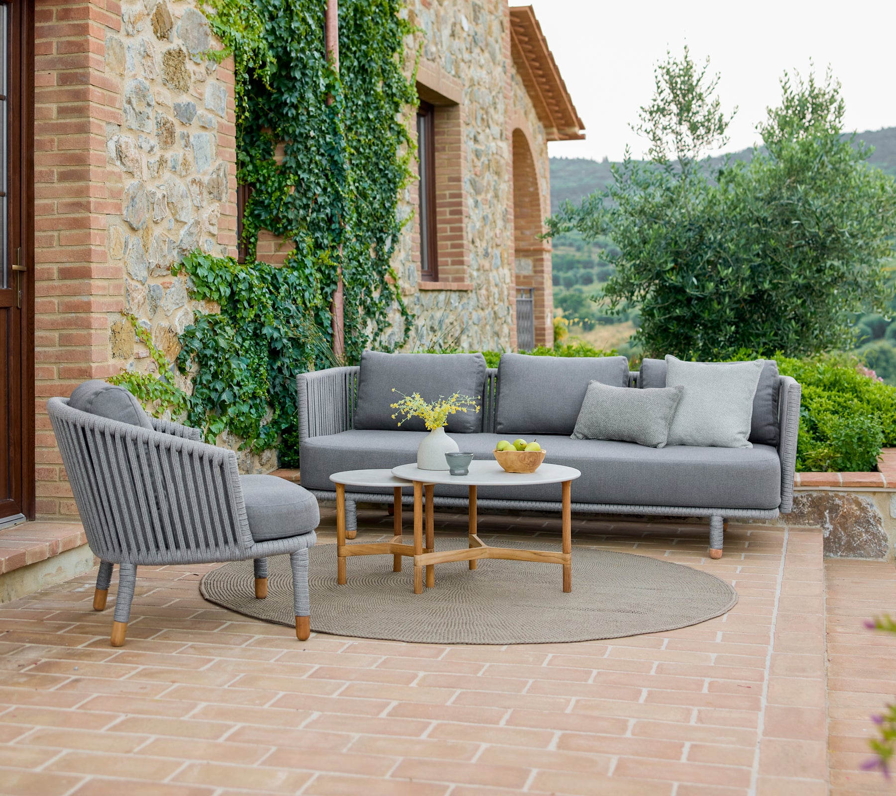 Stylish lounge chair and sofa with a cozy arrangement, accompanied by sleek coffee tables, surrounded by greenery.