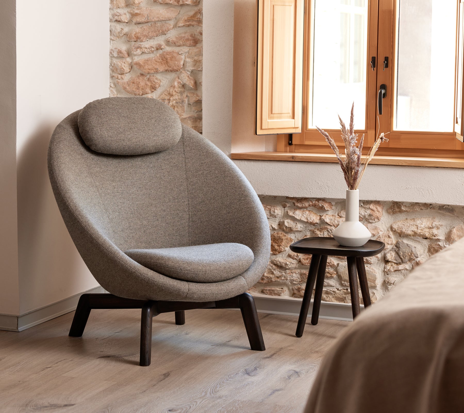 Stylish, curved upholstered chair with a comfortable headrest, accompanied by a small side table featuring a vase and decorative elements.