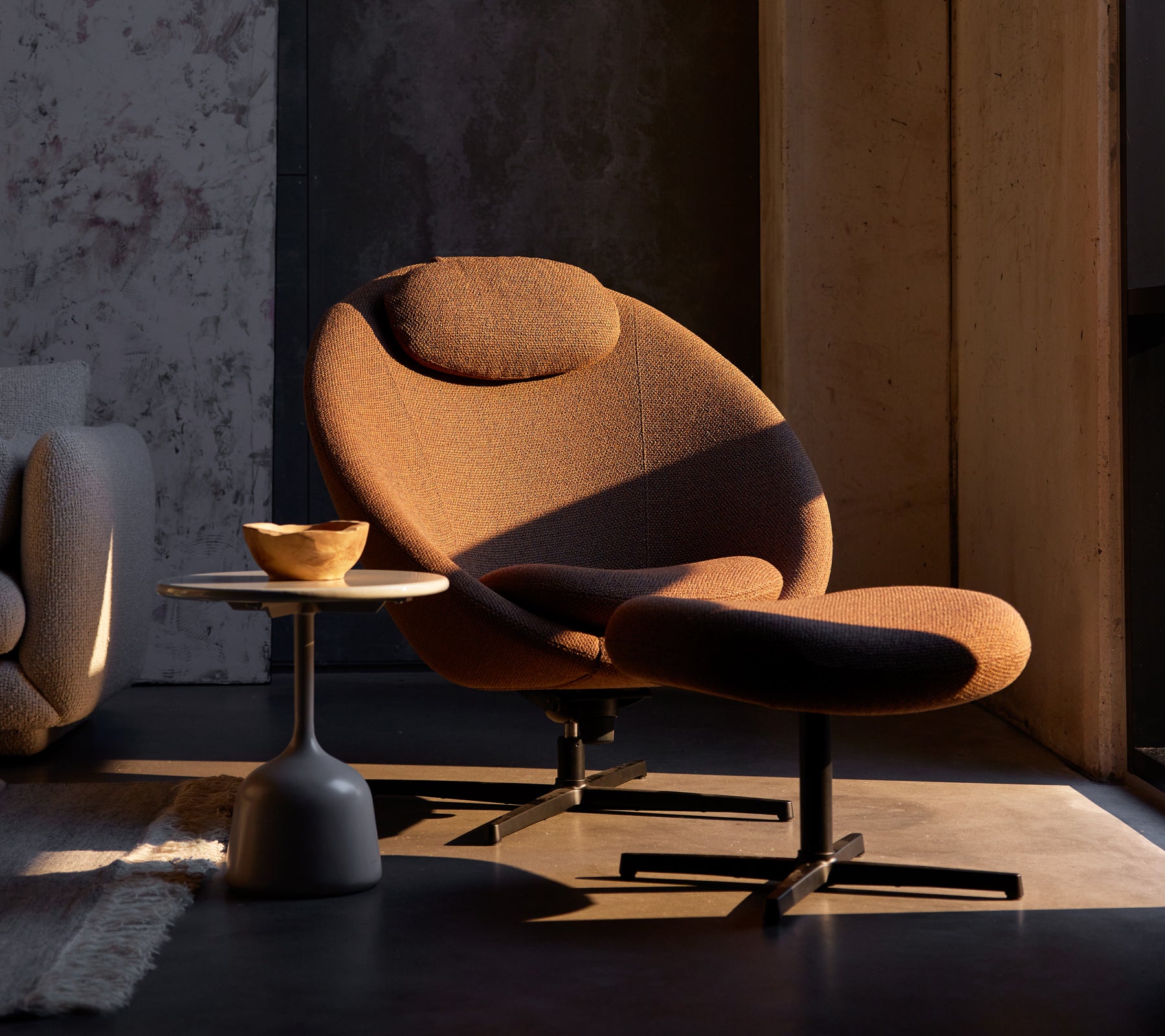Umber brown Pace chair with a matching footstool, complemented by a small side table featuring a wooden bowl.