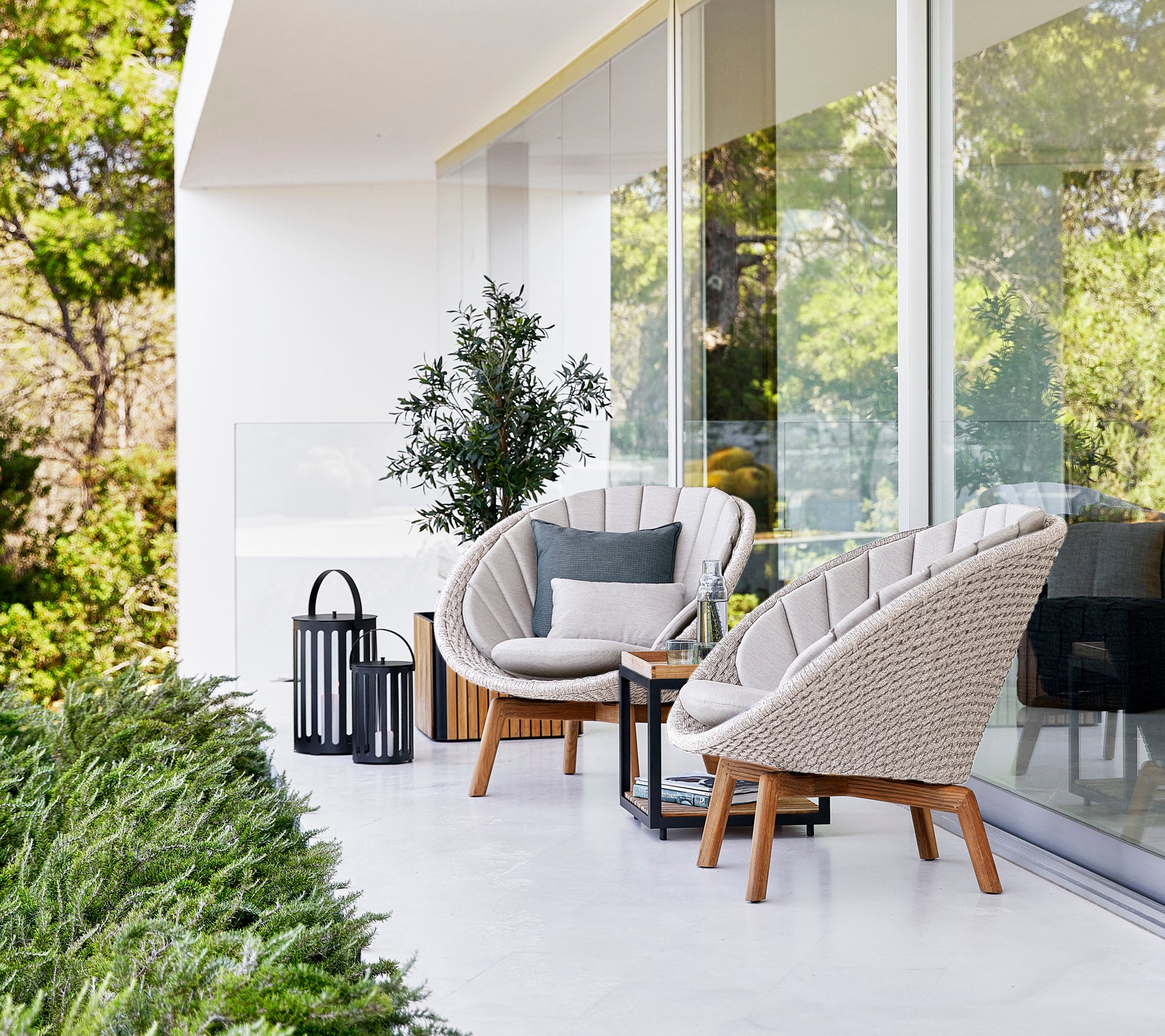 Modern outdoor lounge setting with white chairs, grey cushion, black table, and black lantern.