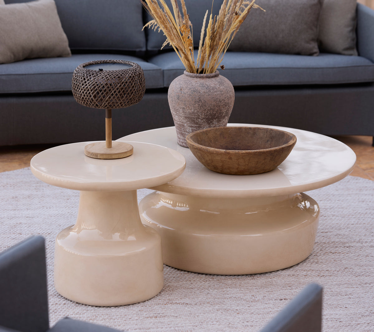 Modern beige coffee and side tables with a brown bowl and metal lamp in a lounge setting.