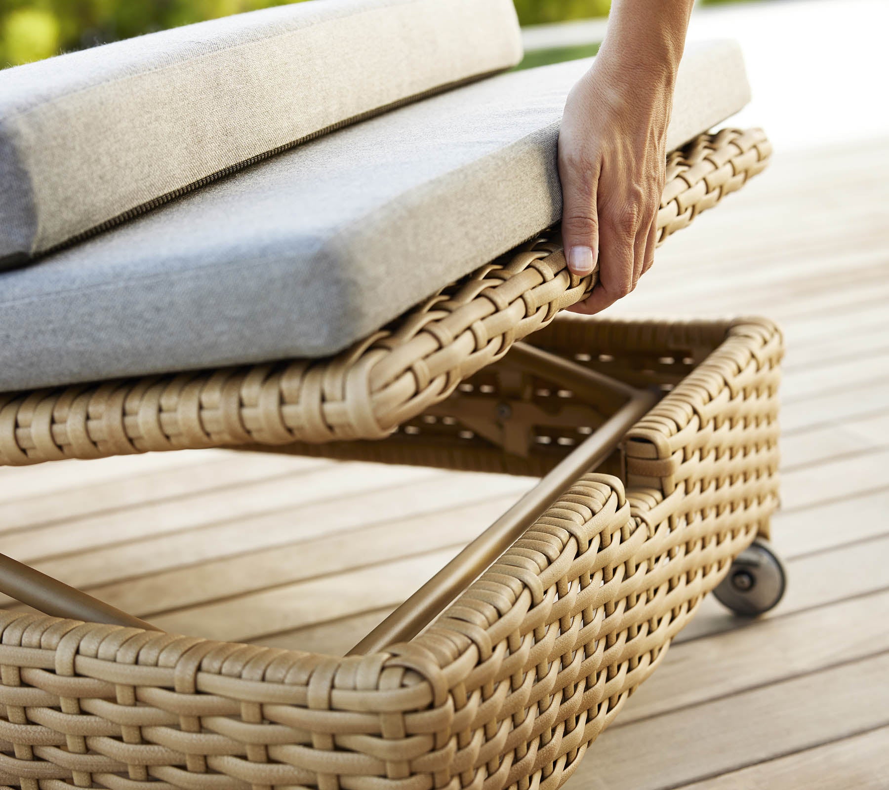 A hand adjusting the cushion on a woven rest sunbed, featuring a stylish design and soft gray upholstery.