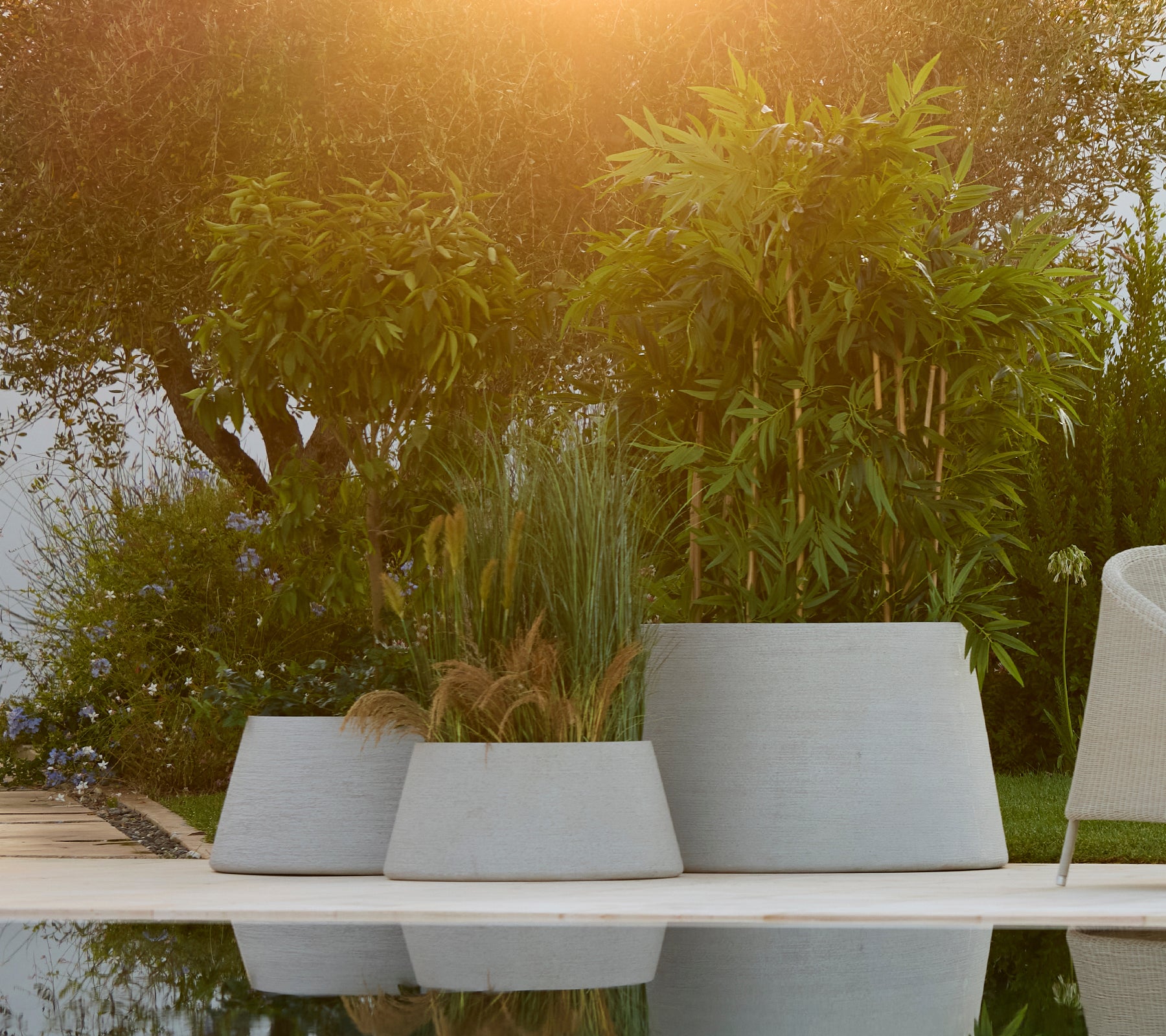 Collection of grey planters arranged in a garden setting with lush greenery.