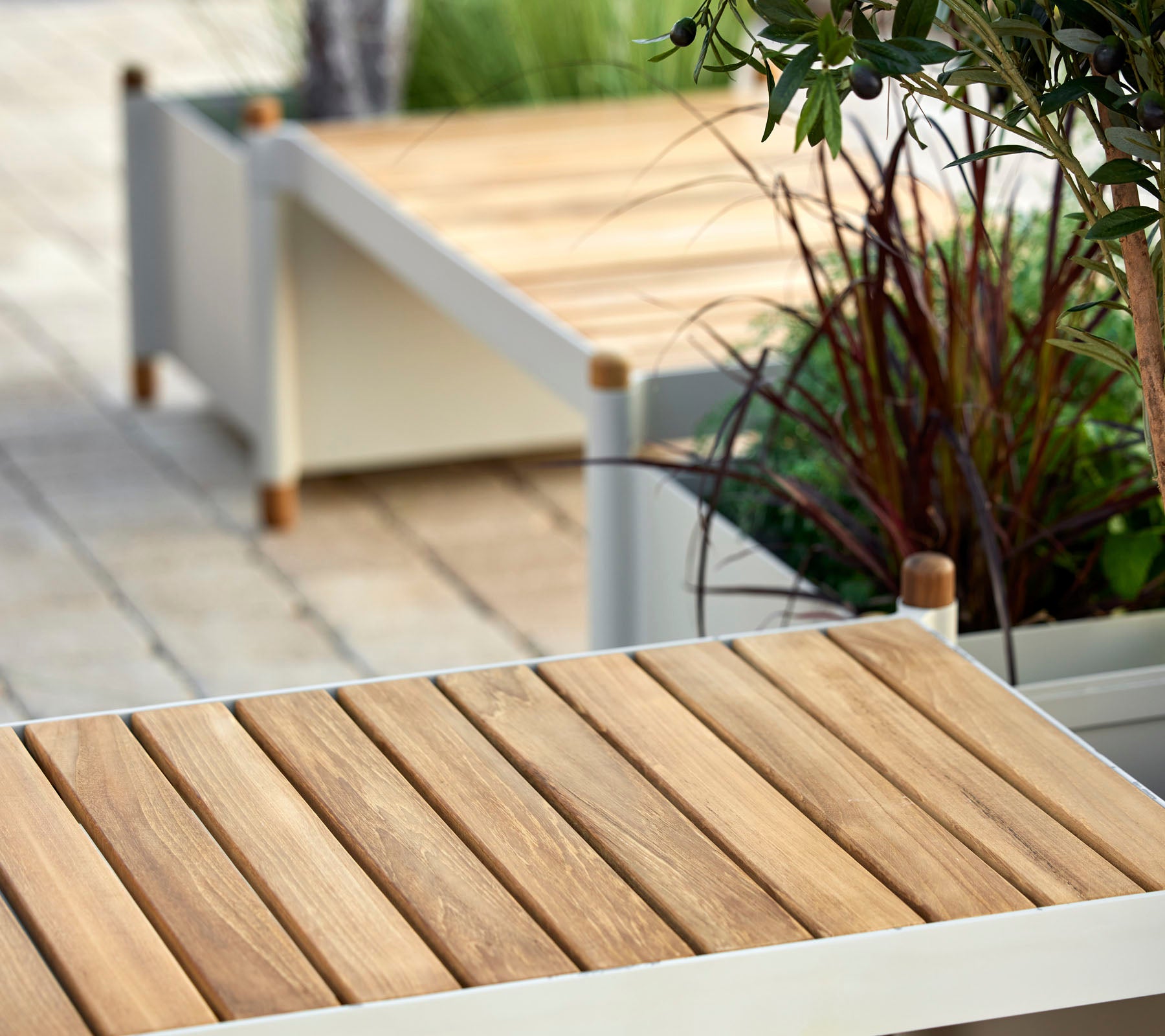 Wooden slatted surface with minimalist design elements, surrounded by greenery and decorative planters.