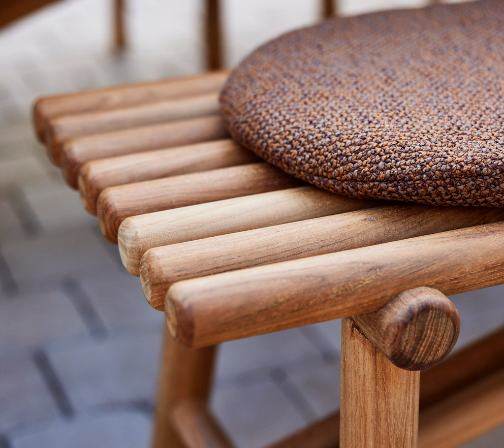 Close-up of a teak bench featuring wooden sticks and a textured round cushion on top, highlighting craftsmanship and natural materials.