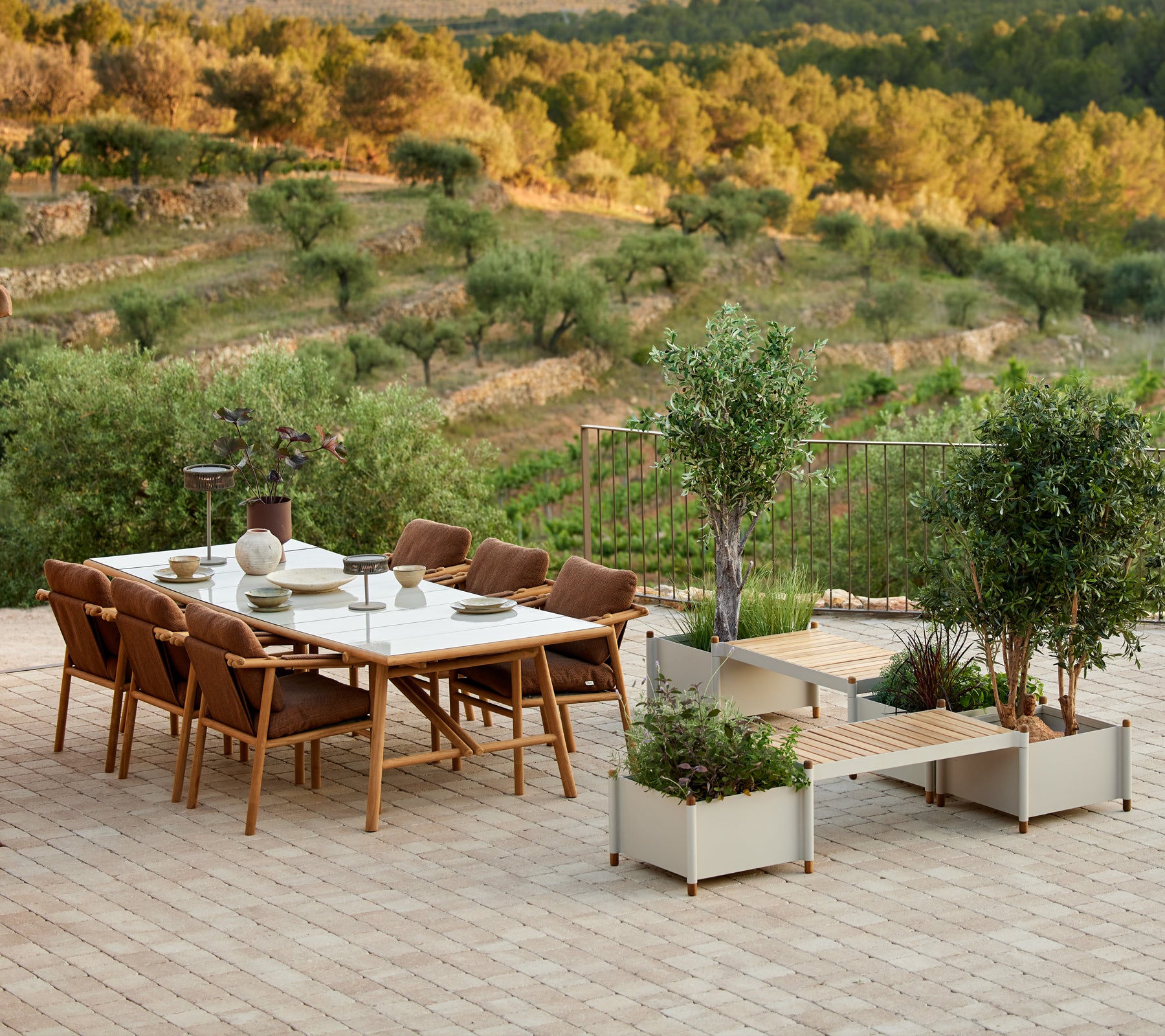 Stylish teak dining set with chairs and a planter bench, surrounded by greenery and scenic landscape.