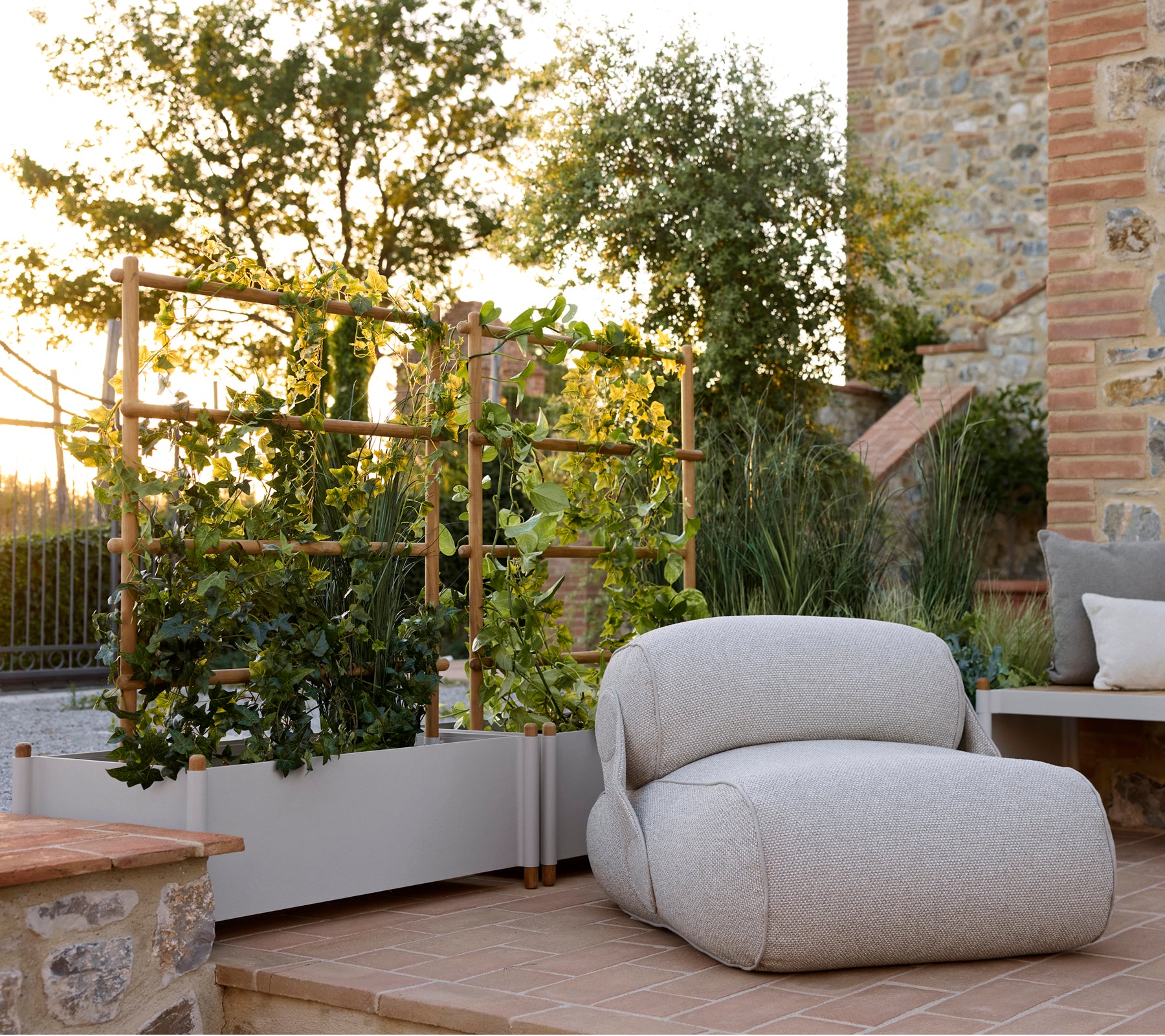 Plush lounge chair beside a stylish planter, featuring greenery and a serene outdoor setting with warm natural lighting.