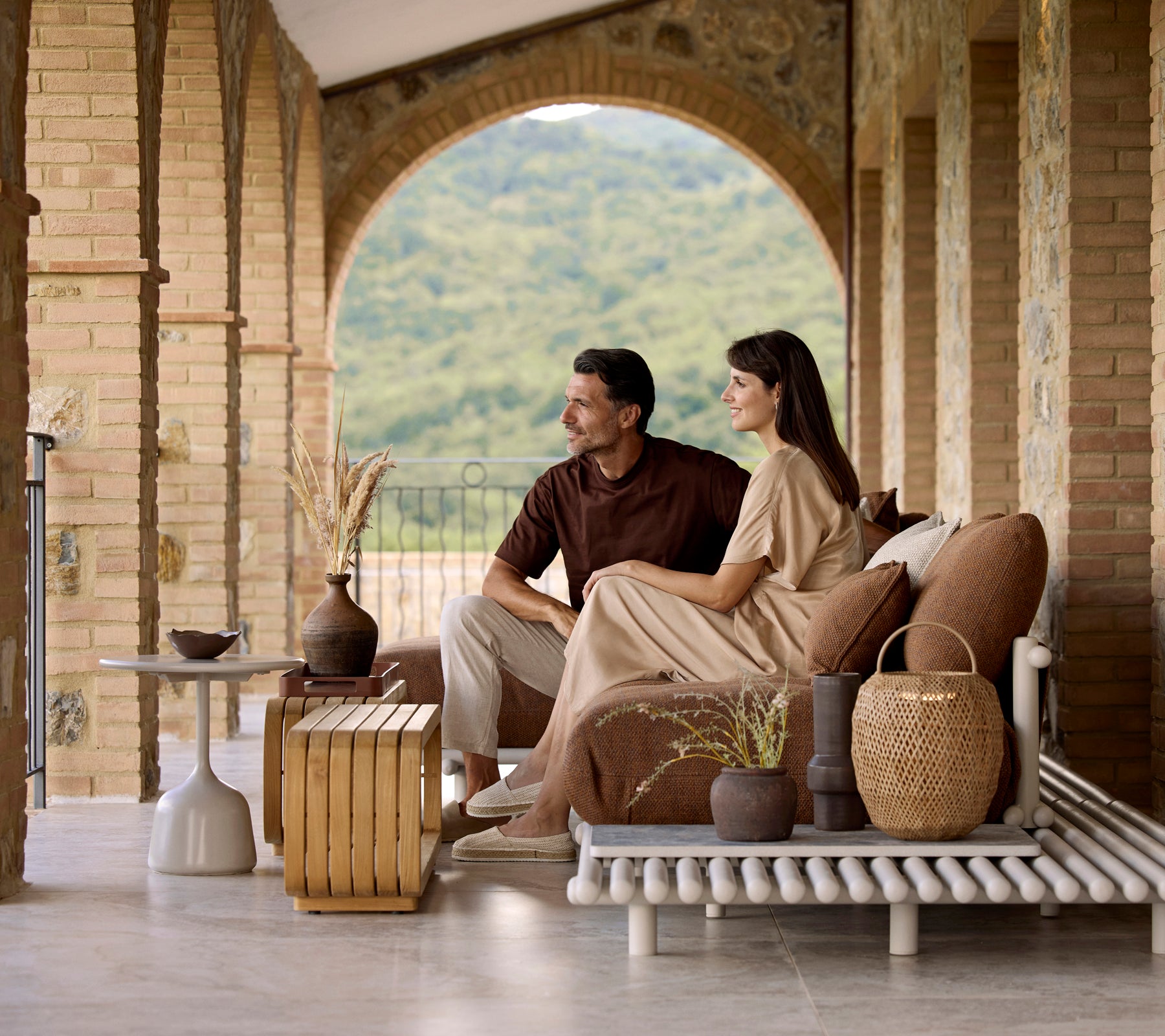 A couple sitting on a stylish sofa, enjoying a Mellow coffee table with decorative items and a serene view in the background.