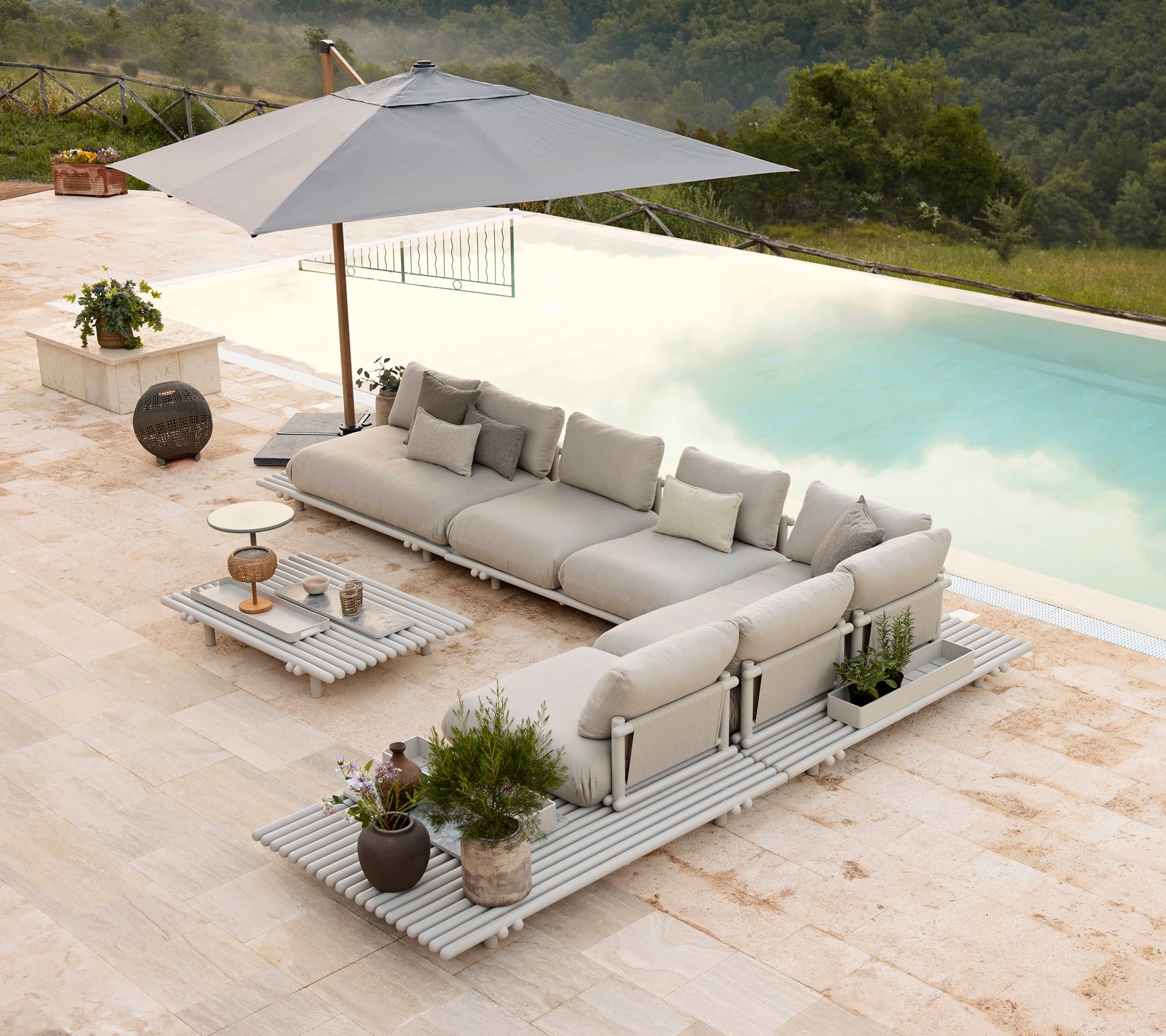 Stylish aluminium lounge set with plush cushions and a matching coffee table, complemented by an umbrella and decorative plants.