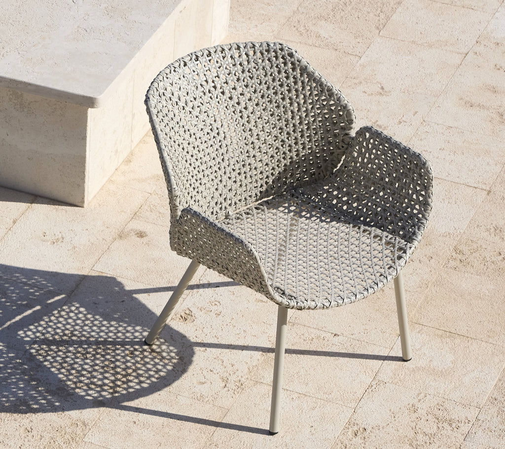 Stylish lounge chair with a woven design and metal legs, casting a shadow on a light-colored surface.