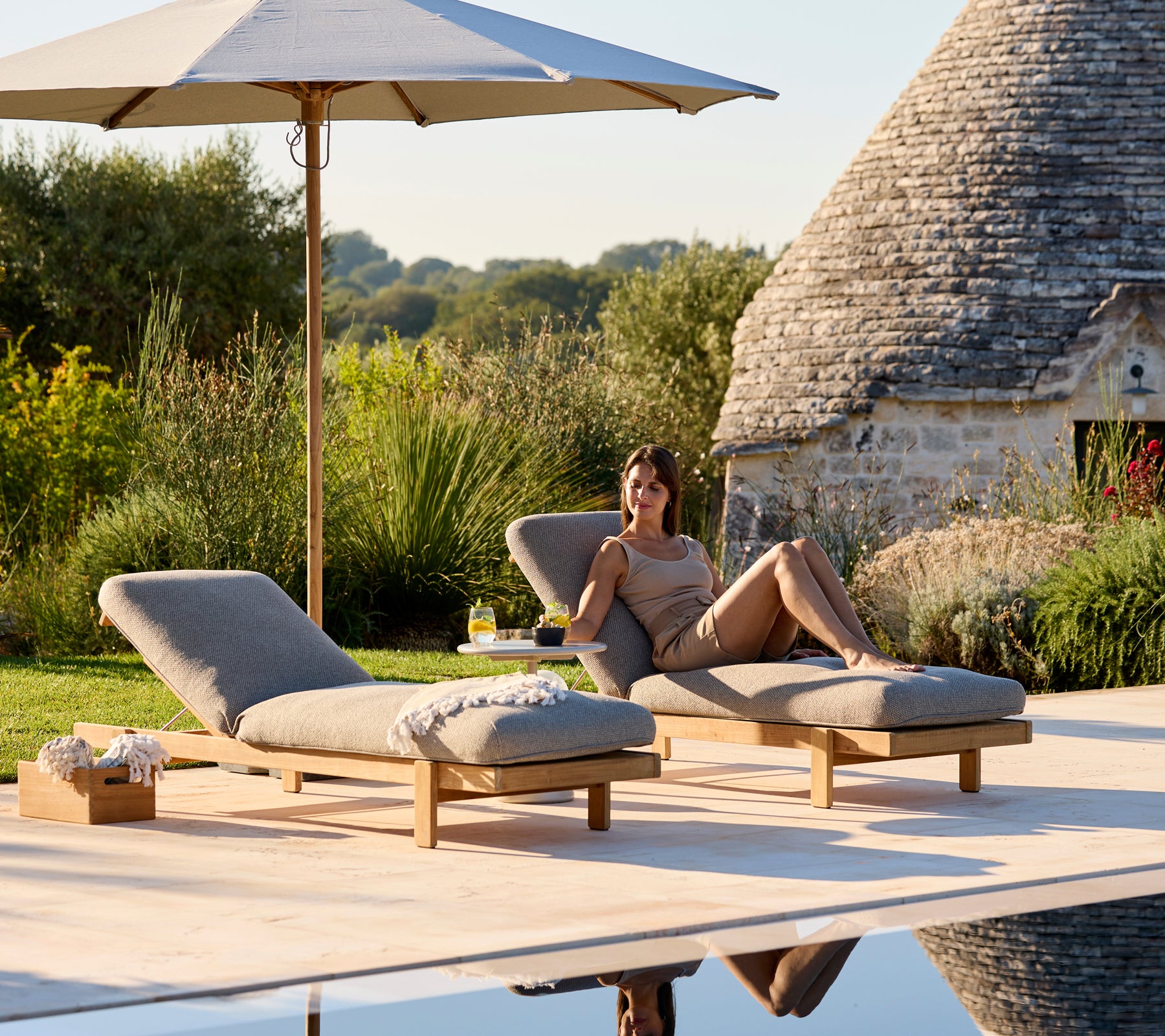 Two loungers with beige cushions under a parasol in a serene outdoor setting.