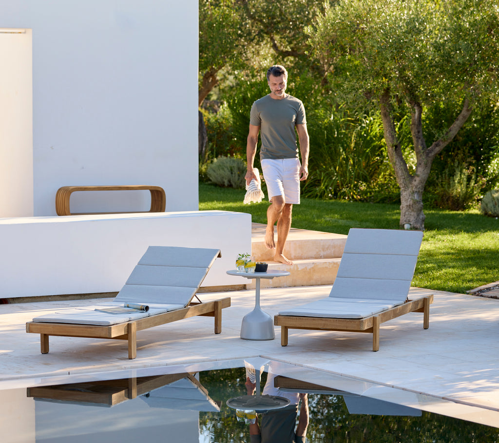 Modern outdoor setting with grey lounge chairs and a white side table by a pool.