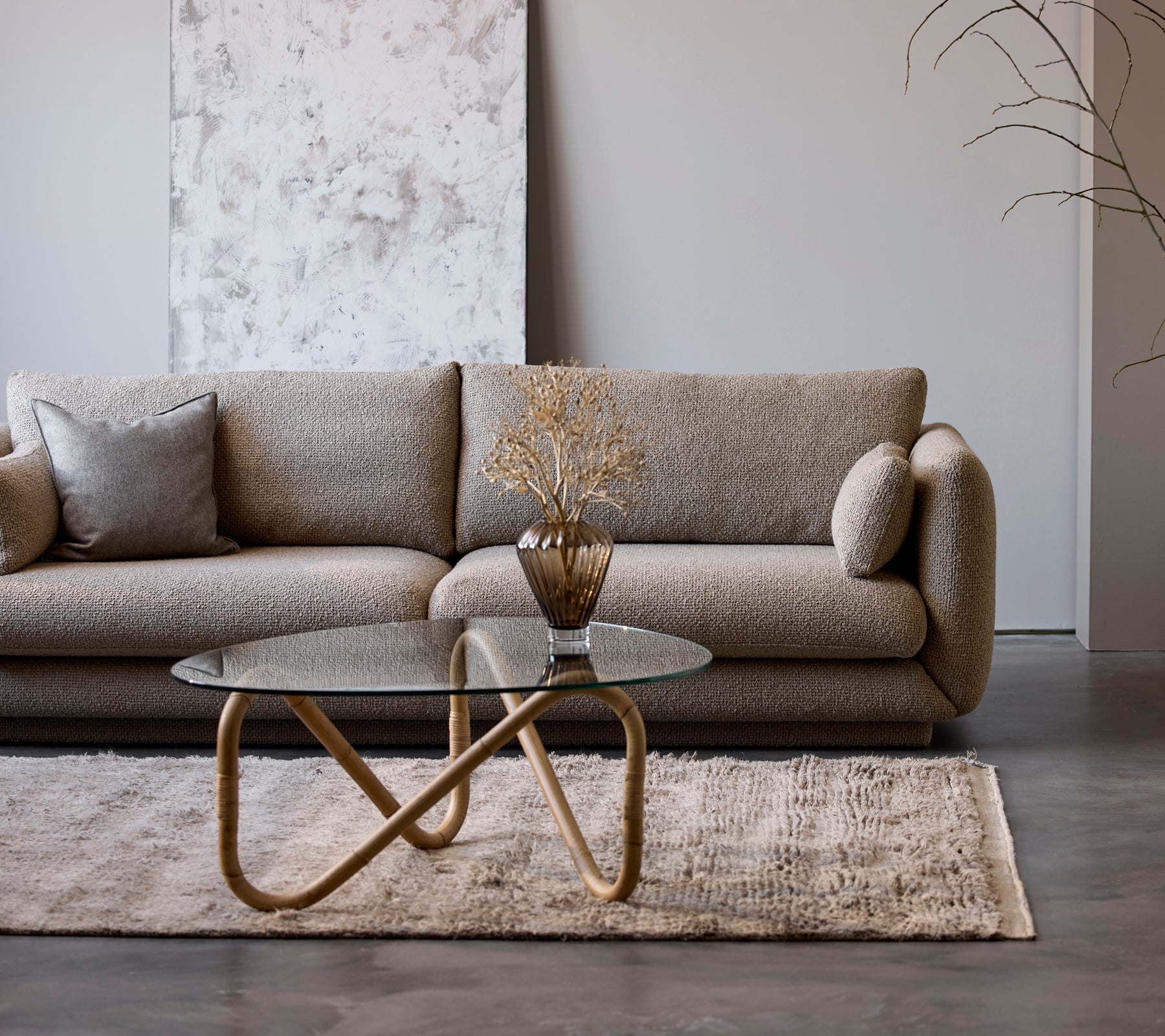 A modern beige sofa with a glass coffee table and a decorative vase in a minimalist lounge setting.