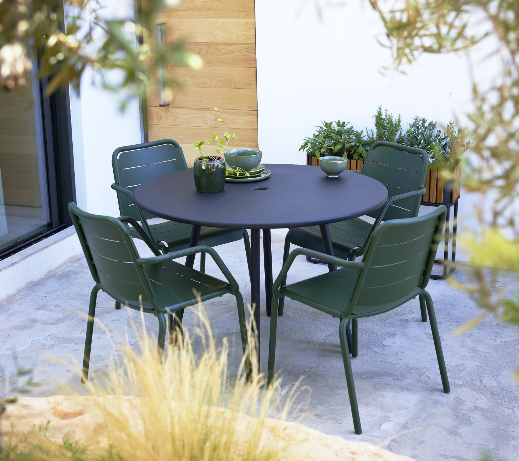 Green Copenhagen armchairs arranged around a round black table, complemented by decorative dishes and plants on the surface.